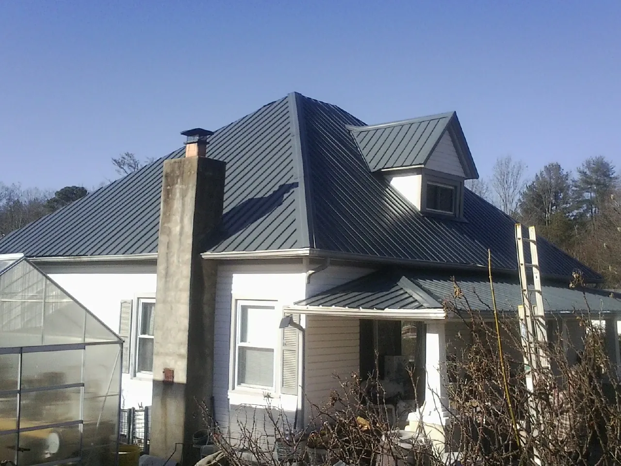 Dark blue standing seam metal roof on a white farmhouse with dormer — Slate & Tile Roof Repair by Roofing Brothers in Greene
