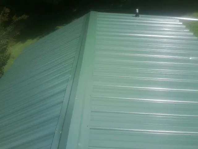 New green metal panels meeting at the ridge of a roof — Flat Roof Repair work by our crew in Greene